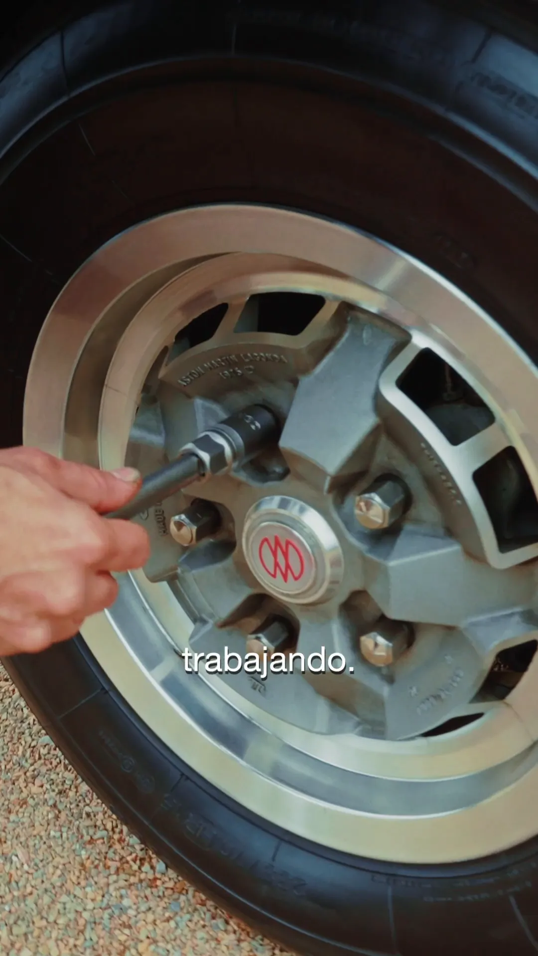 Omar, mecánico, cambia la rueda de un Aston Martin clásico: el taco, el crique y las tuercas.
