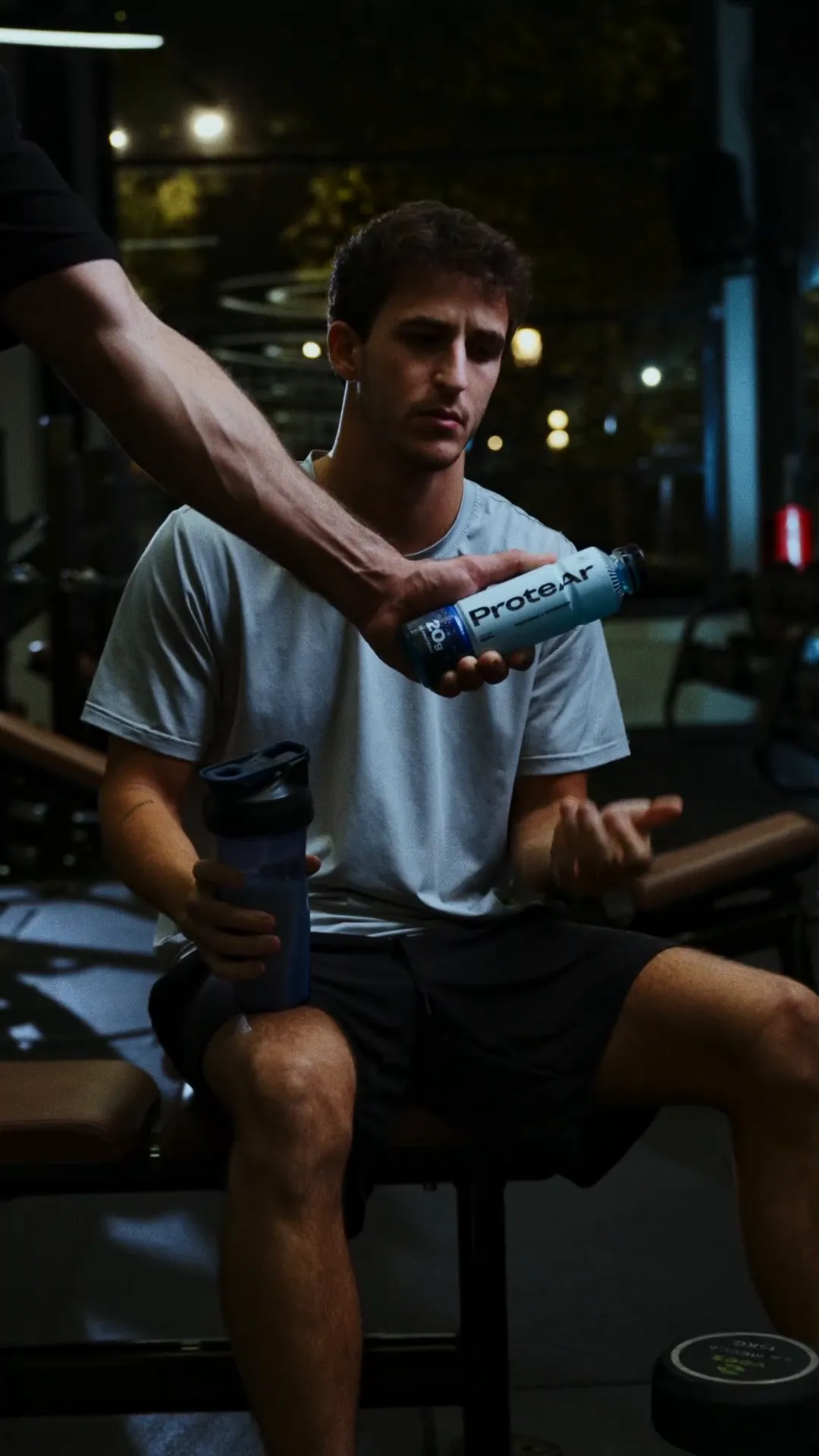 En el gimnasio, un entrenador le alcanza una ProteAr a un chico entre series.
